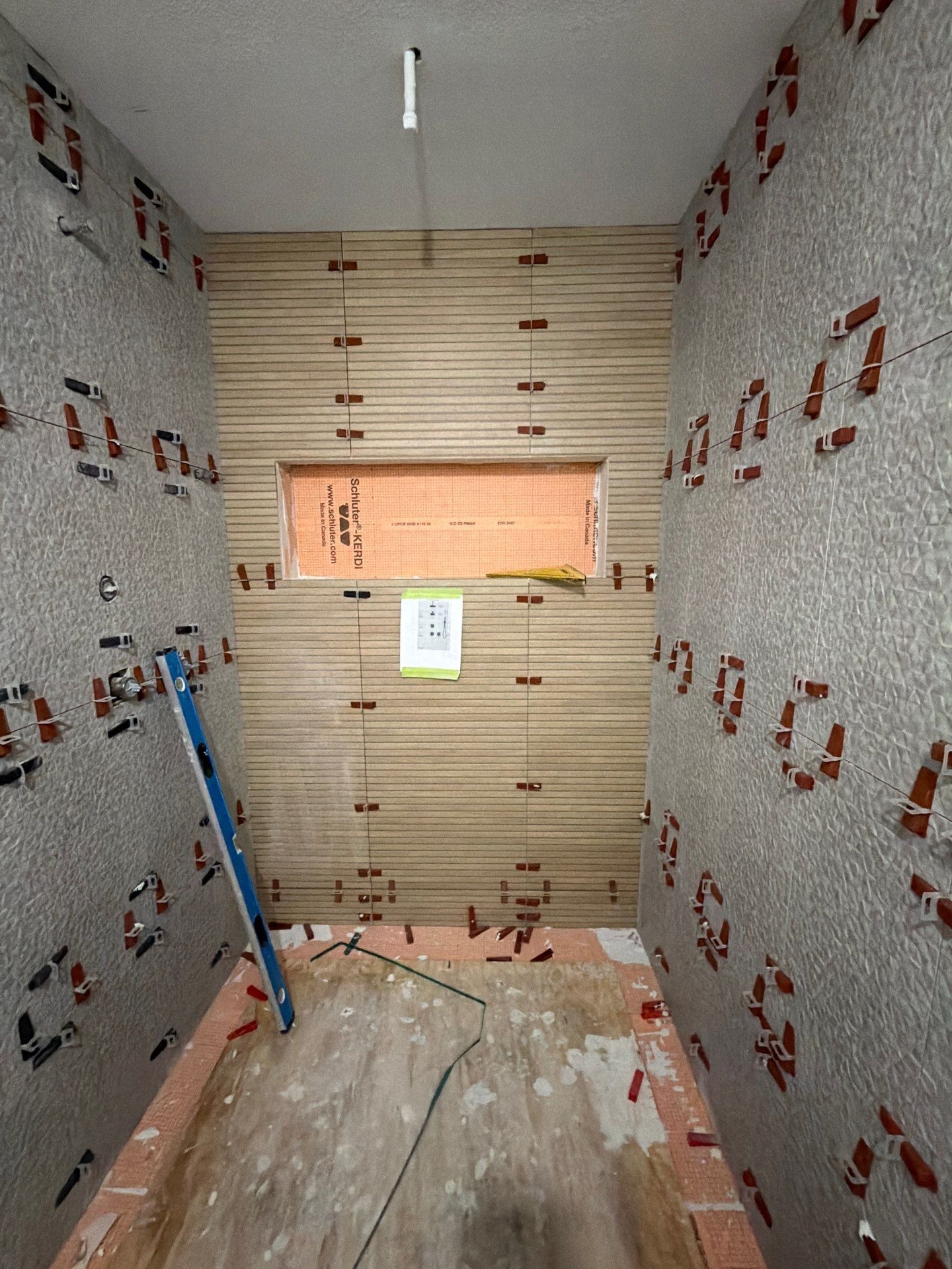 GD Construction walk-in shower mid tile install — large-format tile, textured accent wall, and a built-in niche with leveling clips still set